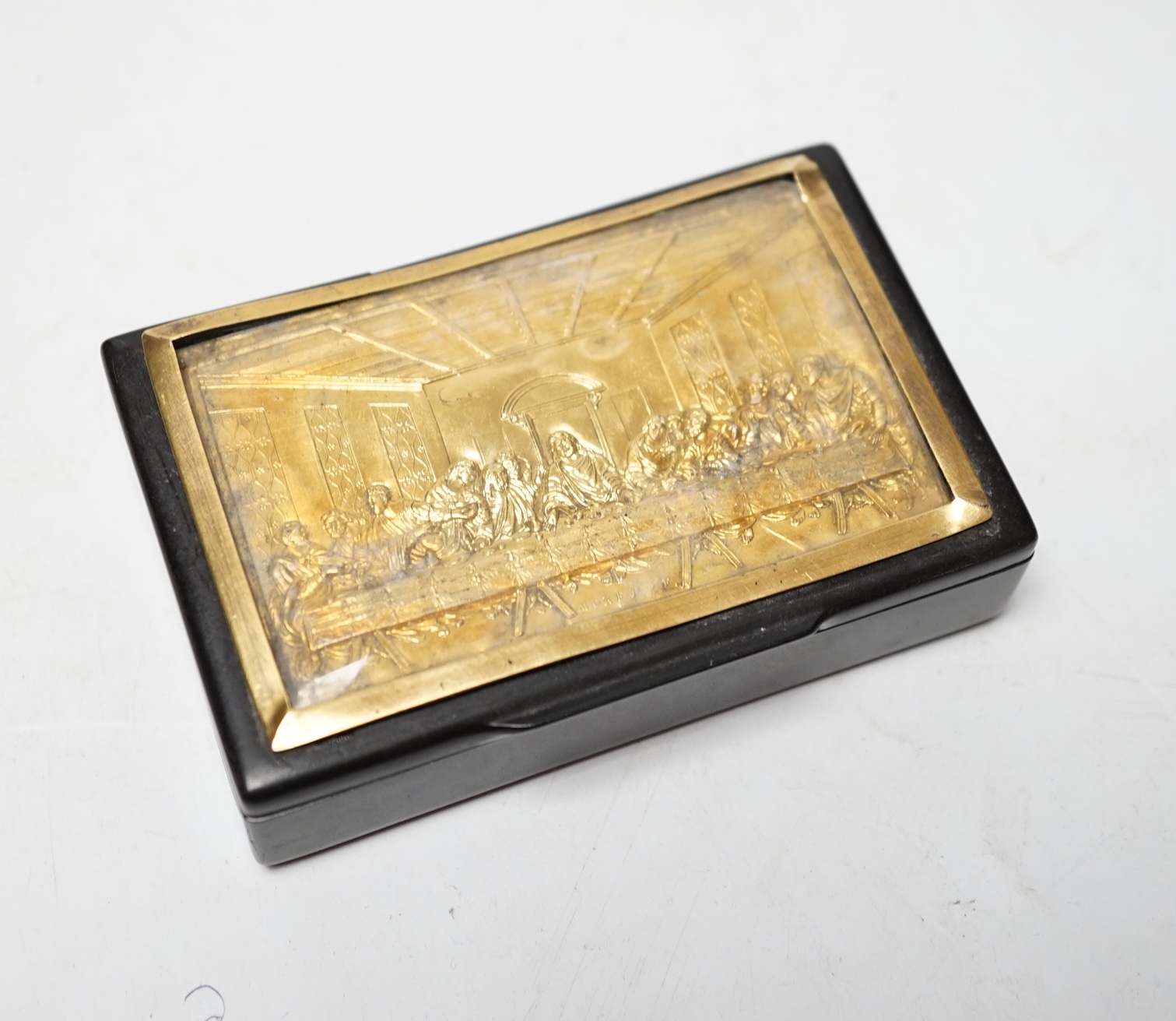 A 19th century ebonised rectangular snuff box, with inset yellow metal lid, with scene depicting The Last Supper after Da Vinci, 92mm. Condition - poor